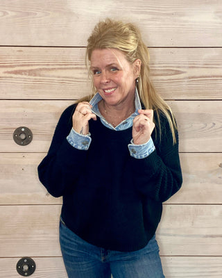 Woman wearing a navy sweater with light blue cuffs and collar against a wooden background
