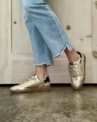 Gold sneakers worn with light blue jeans against a wooden background