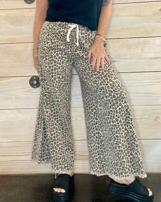 Person wearing a black t-shirt and leopard print pants standing against a wooden wall.
