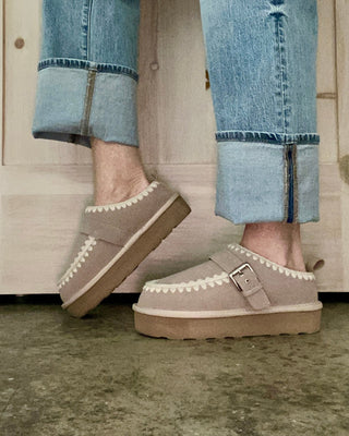 Person wearing beige shoes with brown soles and rolled-up jeans standing on a concrete floor.