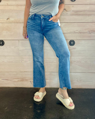 Person wearing a gray t-shirt and blue jeans standing against a wooden wall.