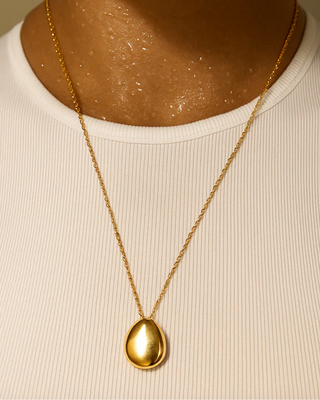 Gold necklace with a pendant on a person wearing a white shirt.