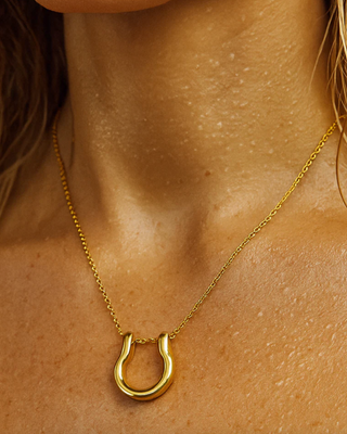 Gold horseshoe necklace on a person's neck