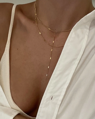 Close-up of a person wearing a delicate gold necklace with a neutral background