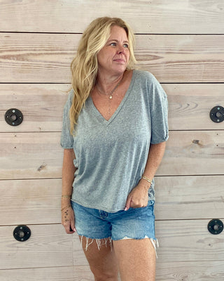 Woman wearing a gray t-shirt and denim shorts standing against a wooden wall.