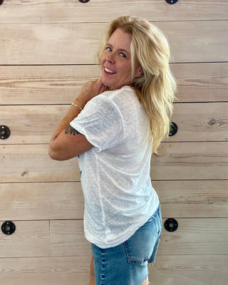 Woman wearing a white t-shirt and denim shorts standing against a wooden wall.