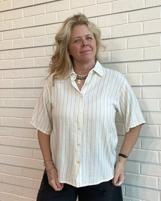 Person wearing a white striped shirt and black pants standing against a light brick wall.