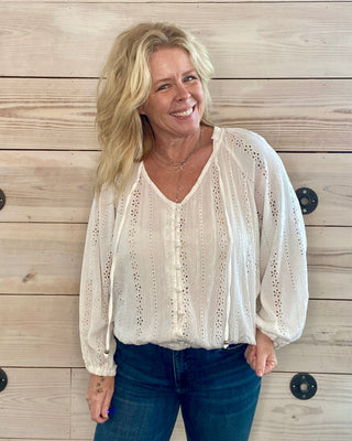 Woman wearing a white blouse with lace details against a wooden wall.