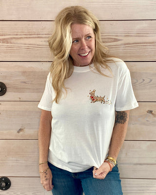 Person wearing a white t-shirt with a design, standing against a wooden background