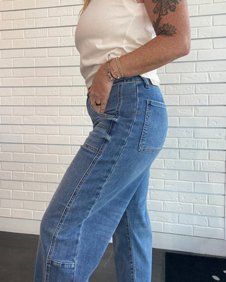A person wearing light blue wide-leg denim jeans and a cream sleeveless top, standing in front of a white brick wall.
