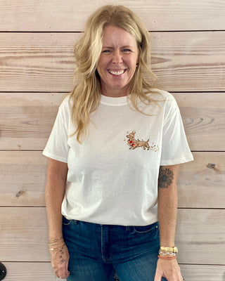 Woman wearing a white t-shirt with a graphic design and blue jeans standing against a wooden wall.