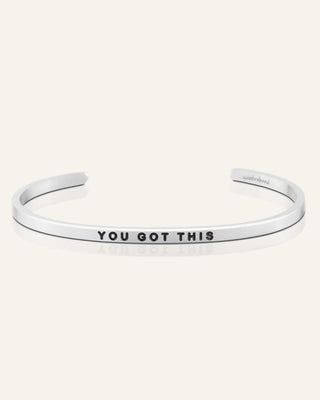 A silver open cuff bracelet with the words 'YOU GOT THIS' engraved in black capital letters on the front, displayed on a light cream background.