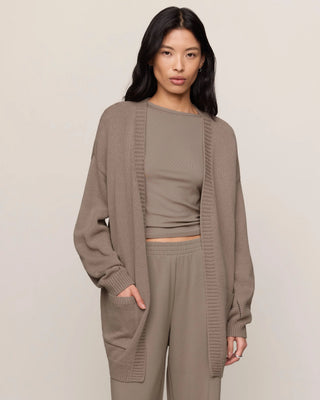 A woman modeling a matching taupe knit loungewear set consisting of a long-sleeve open-front cardigan, a cropped tank top, and wide-leg pants, photographed against a neutral studio backdrop.
