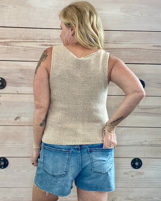 Person wearing a beige sleeveless top and blue shorts against a wooden wall.
