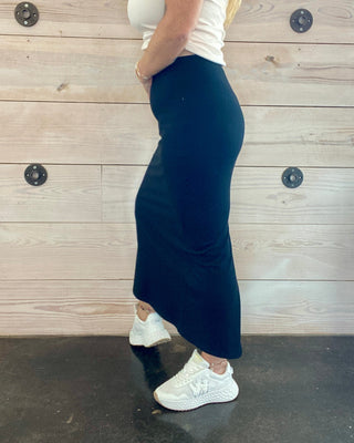 Person wearing a white top and black skirt against a wooden wall.