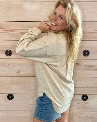 Woman wearing a beige long-sleeve top and denim shorts against a wooden wall.