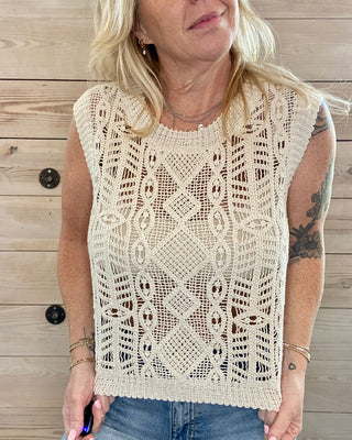 Woman wearing a sleeveless crochet top against a wooden background