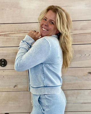 Woman in light blue tracksuit standing against a wooden wall