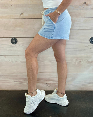 Person wearing a white crop top and light blue shorts against a wooden background