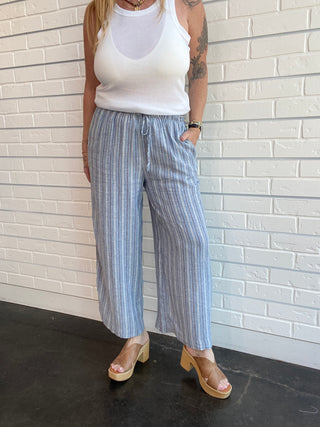 Person wearing a white tank top and blue striped pants against a white brick wall.