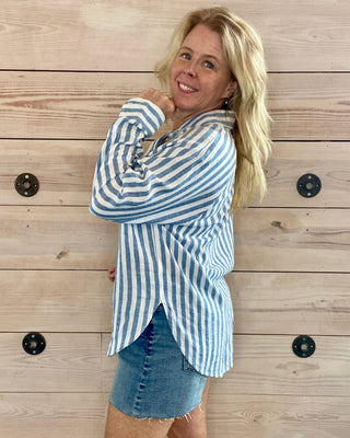 Woman wearing a blue and white striped shirt and denim skirt against a wooden background