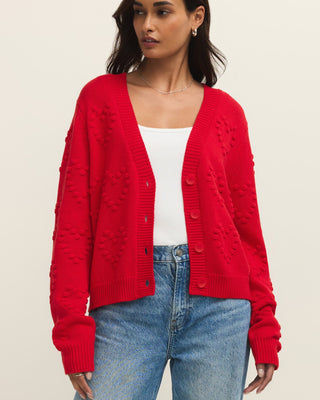 Woman wearing a red cardigan over a white top and blue jeans on a beige background