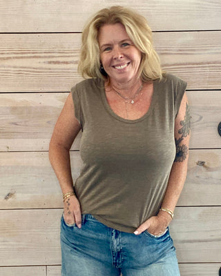 Woman wearing a sleeveless top and denim shorts standing against a wooden wall.