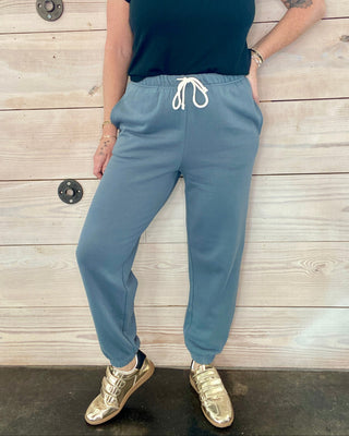 Person wearing a dark shirt and light blue sweatpants against a wooden background