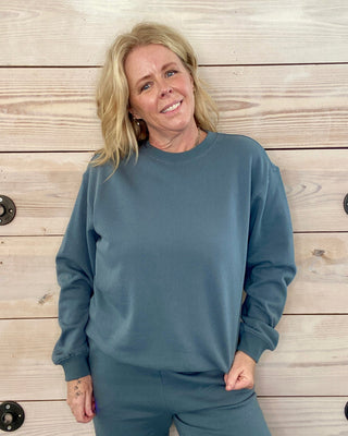 Woman wearing a blue sweatshirt and pants against a wooden background
