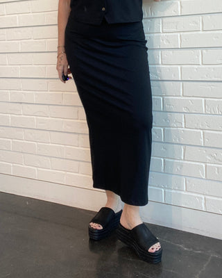 Woman in a black outfit standing against a white brick wall.