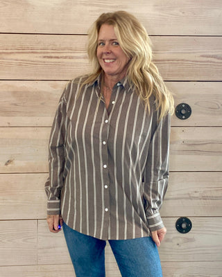 Woman wearing a striped shirt and jeans standing against a wooden wall.