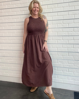 Woman wearing a brown dress standing against a white brick wall.
