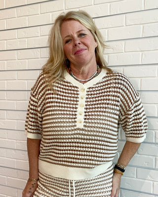 Woman wearing a brown and white striped outfit standing against a light brick wall.