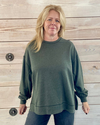 Person wearing a green sweatshirt standing against a wooden wall.