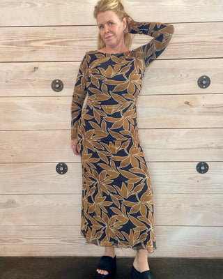 Woman wearing a patterned dress against a wooden wall.