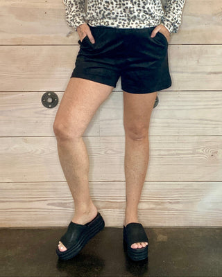 Person wearing a leopard print top and black shorts against a wooden wall.