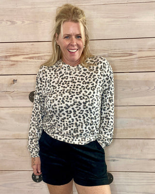 Woman wearing a leopard print top and black shorts standing against a wooden wall.