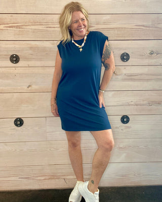 Woman wearing a blue dress standing against a wooden wall.