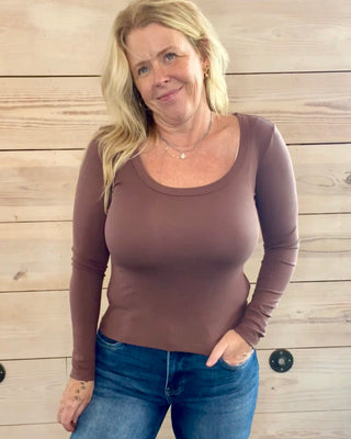 Woman wearing a brown long-sleeve top and blue jeans against a wooden background
