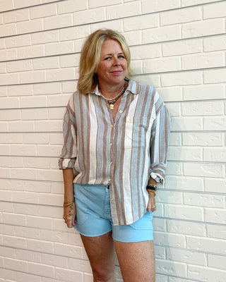 Woman wearing a striped shirt and light blue shorts standing against a white brick wall.