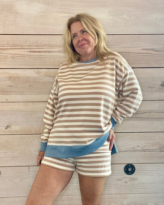 Person wearing a striped sweater and shorts set against a wooden wall.