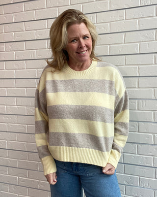 Woman wearing a striped sweater and jeans standing against a light brick wall.